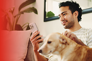 Portabilidad a Claro Costa Rica con 75% de descuento Hombre usando su celular en el sillón junto a su perro después de pasarse a Claro con su mismo número